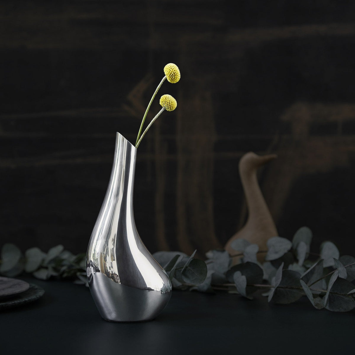 VAGNBYS Swan Solitaire Vase holding two yellow flower stems on a dark table